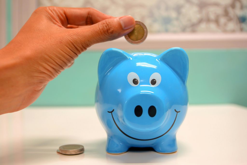 pexels photo 1602726 1602726 Hand inserting a coin into a blue piggy bank for savings and money management.